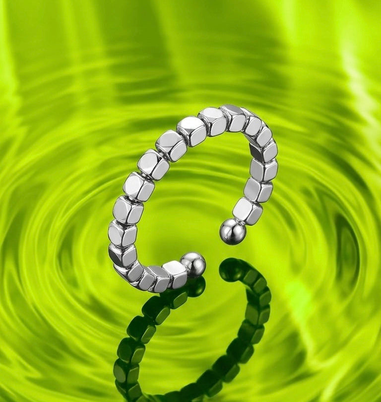 Silver metal ring with square bead design floating on a neon green rippling pool